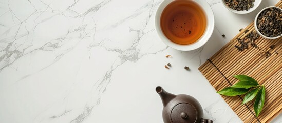 Poster - Top down view of a setup on a white marble surface with a bamboo mat dry tea leaves a teapot and space for text or images. Creative banner. Copyspace image
