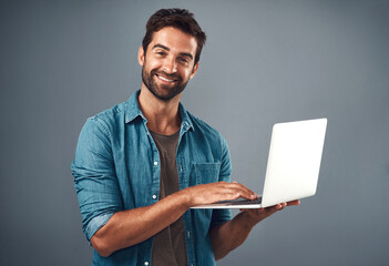 Fototapete - Laptop, happy and portrait of man in studio with research for creative software with project development. Smile, technology and graphic designer work on multimedia art on computer by gray background.