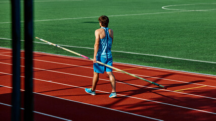 Pole vaulter in blue tank top, young athletic man walking at outdoor standing with pole, getting ready for intense training session. Sport, competition, tournament, active lifestyle, strength concept