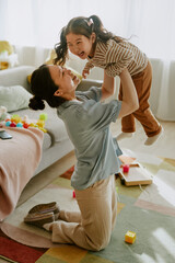 Young Asian mom lifting her daughter who laughing loudly