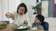© Marco - Grandmother helps grandson with his meal at the dining table, cutting food for young boy, moment of family togetherness and nurturing. bond between generations during mealtime