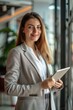 © vefimov - A young, smiling woman in a business suit using a tablet.