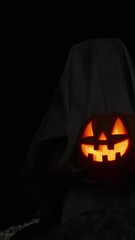 Wall Mural - Vertical video. A Ghost in a Dark Cave by the Sea Holds a Jack-O'-Lantern Pumpkin with Burning Flame Inside. Candles in the Cave Illuminate the Walls. Ominous All Saints' Day Atmosphere.