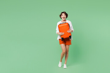 Wall Mural - Full body happy surprised shocked traveler woman wear casual clothes hold suitcase bag look camera isolated on plain green background. Tourist travel abroad in free time rest. Air flight trip concept.