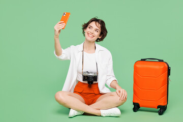 Wall Mural - Full body traveler woman wear casual clothes sit near suitcase bag do mobile cell phone selfie shot isolated on plain green background. Tourist travel abroad in free time rest Air flight trip concept