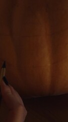 Wall Mural - Vertical video. In the Dark with Flickering Candlelight, a Woman Draws Mouth and Eyes on a Pumpkin for Halloween, Close-Up.