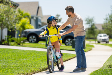 Canvas Print - Happy Fathers day. Father and son in bike helmet for learning to ride bicycle at park. Father helping son cycling. Father and son on the bicycle on summer day. Kid son trying to ride bike with father.