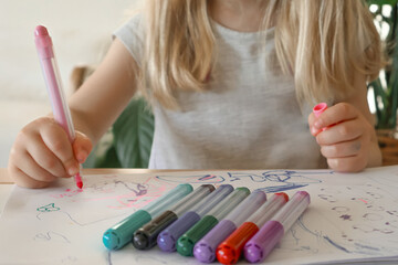 Little blonde girl draws a picture with multi-colored markers. Preschool education.