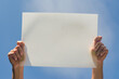 © SheyninaY - male hands hold white empty poster on blue sky background . High quality photo