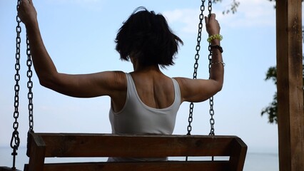 Happy woman ride on swing at tropical at sea beach. Carefree lady enjoying rest near ocean. Adult female having fun at sea shore. Concept of summer vacation or holiday. Close up Slow mo