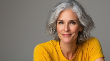 Close up of mature woman with white skin, grey short hair, wavy hair and a clear yellow t shirt, isolated in a light grey studio. Portrait person.