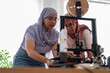 © Studio Marmellata - Two women in hijabs collaborate on a 3D printing project, carefully examining the printer and its outputs. They are focused and engaged, showcasing teamwork and innovation in technology.