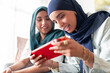 © Studio Marmellata - Two women in hijabs smile as they play a game on a tablet. Their expressions show joy and engagement, highlighting a fun and relaxed atmosphere with modern technology.