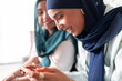 © Studio Marmellata - Two women in hijabs enjoy playing a game together on a tablet. Their smiles and engagement show a shared moment of fun and connection through modern technology.