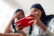 © Studio Marmellata - Two women in hijabs smile as they play a game on a tablet. Their expressions show joy and engagement, highlighting a fun and relaxed atmosphere with modern technology.