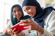 © Studio Marmellata - Two women in hijabs smile as they play a game on a tablet. Their expressions show joy and engagement, highlighting a fun and relaxed atmosphere with modern technology.