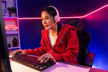 Host channel of beautiful Asian girl streamer concentrating online game wearing headphones pastel color talking with viewers media online. Esport skilled team players in neon blue room. Stratagem.