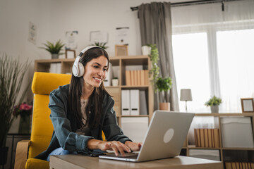 Wall Mural - Adult caucasian woman with headphones listen to music and use laptop