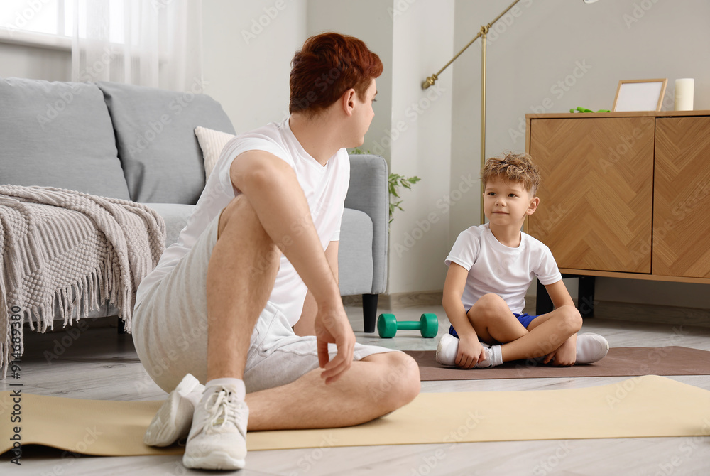 Sporty young man with his little son training at home
