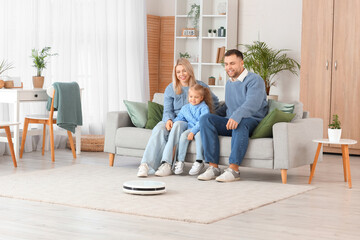 Poster - Happy family with robot vacuum cleaner sitting on sofa at home