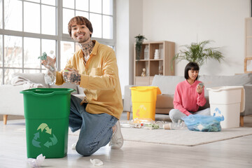 Wall Mural - Young couple with garbage containers sorting rubbish in living room. Recycling concept