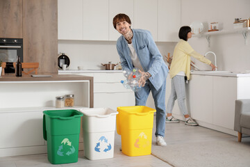 Wall Mural - Young couple with garbage containers sorting rubbish in kitchen. Recycling concept