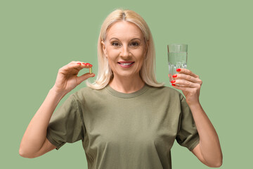 Canvas Print - Mature woman with fish oil pill and glass of water on green background