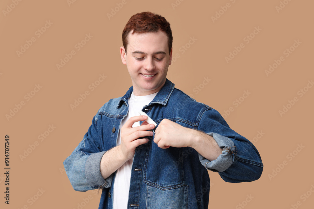 Handsome young man with lip balm in jeans jacket pocket on brown background