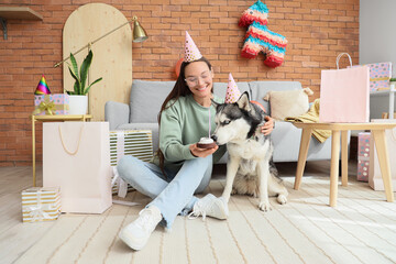 Wall Mural - Young woman and cute husky dog with party hats and cake at home. Birthday celebration