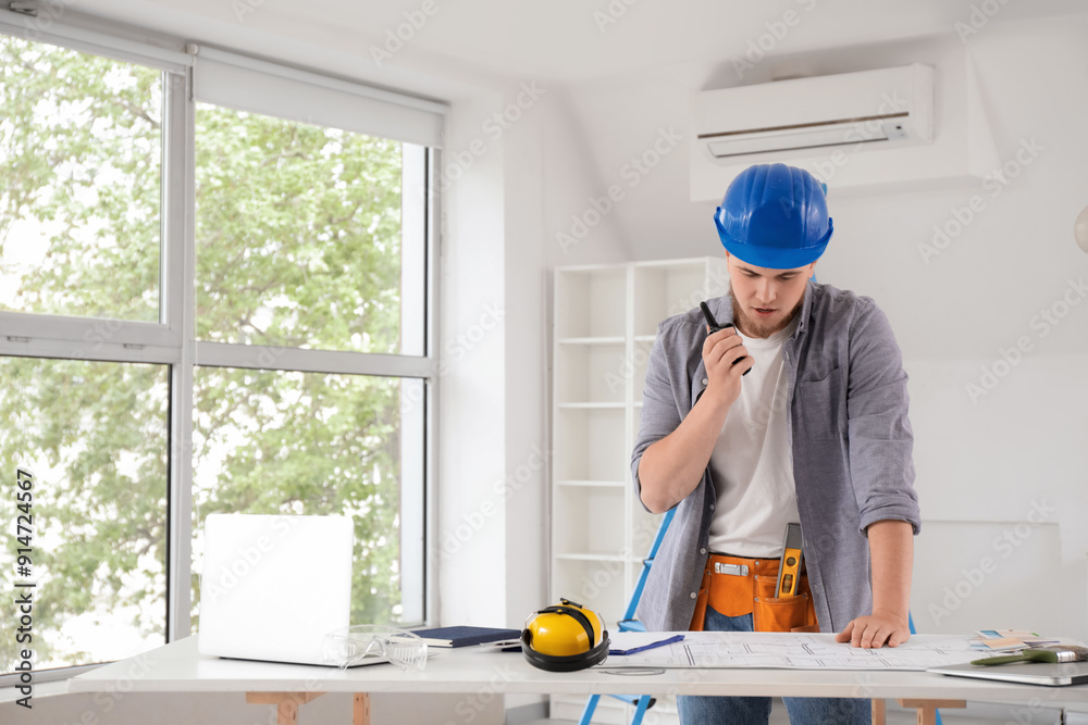 Male contractor with house plan talking on radio transmitter in room