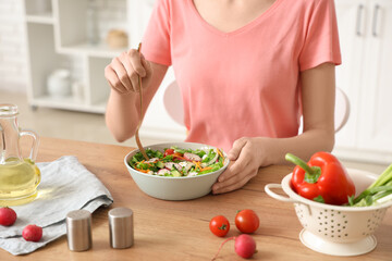 Poster - Young woman with bowl of fresh vegetable salad at table in kitchen