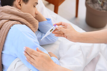 Wall Mural - Mother with thermometer measuring her ill son's temperature in bedroom, closeup