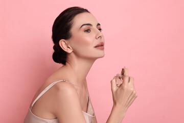 Wall Mural - Beautiful woman with bottle of perfume on pink background