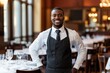 © Veronika - African American waiter standing in restaurant and smiling.