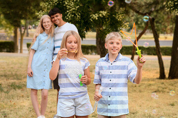 Poster - Happy couple hugging and their cute children blowing soap bubbles in park