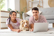 © Pixel-Shot - Young couple with cute dog using laptop on floor at home