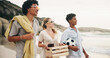 © AzeemudDeen/peopleimages.com - Friends, smile and walking on beach for picnic with basket, beer and fun on travel vacation in summer. Men, girl and together by ocean with alcohol for drinking, conversation and bonding on holiday.