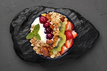 Wall Mural - bowl of oat granola with yogurt, fresh mulberry, strawberries, kiwi mint and nuts on the black rock board