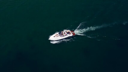 Wall Mural - Flying over a white yacht in motion. White big boat movement on dark blue water aerial view. High-speed motor boat with people moving on the water.