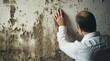© YONG - A man in white shirt, looking at the wall with black mold on it and touching one of them by hand.