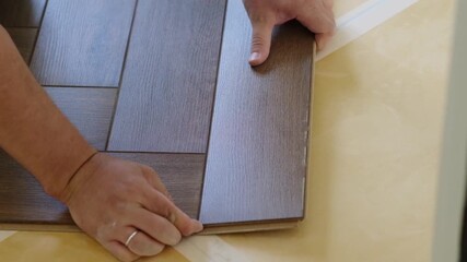 Poster - Man kneeling and installing wood laminate floor in a home. Closeup on male hands. Laying laminate flooring in a new apartment. DIY repair. 