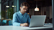 © halo - portrait of a businessman working on a laptop in a modern office, wearing a blue shirt and glasses.