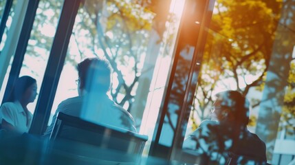 Sticker - A group of people engaged in a relaxed conversation at a sunlit cafe, with reflections of trees and light creating a serene atmosphere.