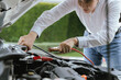 © NanTua - A mechanic uses red and black jumper cables to connect a dead car battery to a power source. The vehicle, with its hood open, undergoes an inspection for electrical issues during a roadside repair.