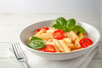 Delicious pasta with aromatic basil and tomatoes close-up on a dish on a wooden board.