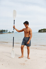 Wall Mural - Active Asian Man Enjoying Sunset Paddleboarding Adventure at the Beach