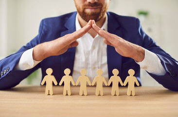 Man hands above small wooden toy human figures on desk to promote, protect human rights, political, cultural freedom protection and safe community of people, civil respect, laws and service to help 