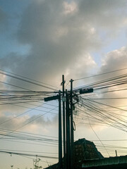 aesthetic view of two electricity poles in the afternoon under a thick cloudy sky. dangerously chaotic power lines in the middle of the city. power line cable on twilight sky. Low angle