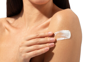 Young woman moisturizing her shoulder with her hand using cream isolated on beige background. Skin care concept