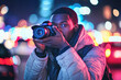 © lenblr - Photographer is framing a night shot in a city with bokeh lights in the background